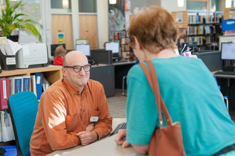 Staff interacting with person at the information desk at Tommy Douglas Library
