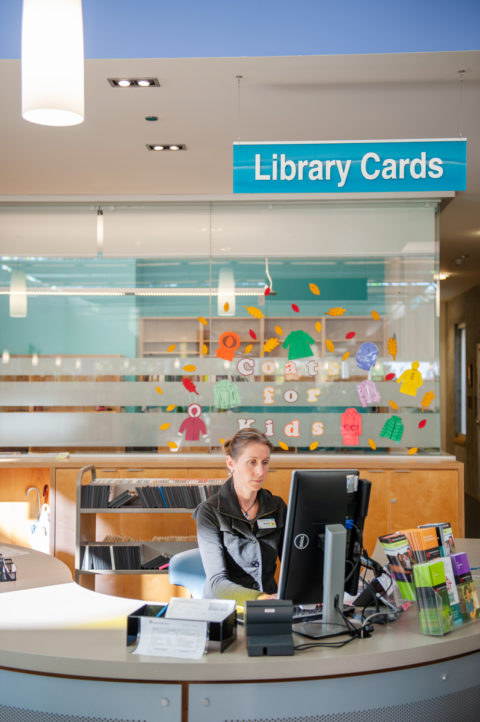 Staff behind a desk with a sign that reads "Library Cards" above them at the Tommy Douglas Library